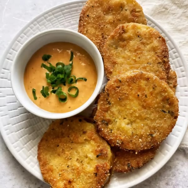Golden-brown fried green tomatoes with a side of creamy orange dipping sauce topped with chives.