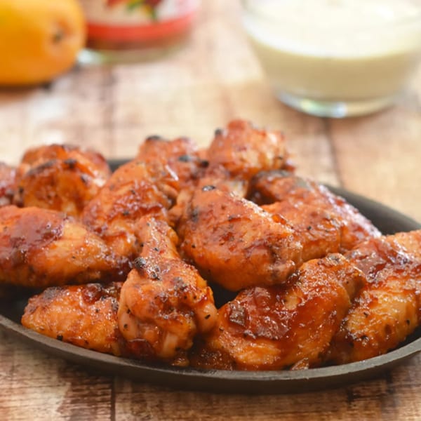 A platter of glistening, golden-brown chicken wings, with a bowl of dipping sauce in the background.