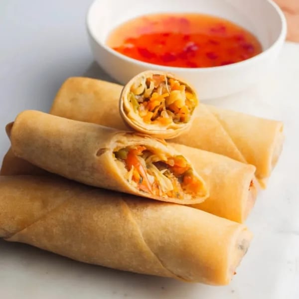 Crispy golden spring rolls, one cut open to show vegetable filling, with a side of sweet chili sauce.