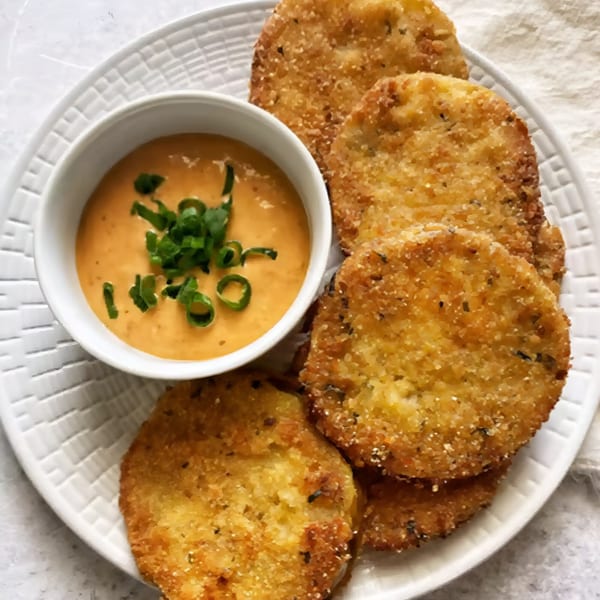 Golden-brown fried green tomatoes with a side of creamy orange sauce topped with green onions.