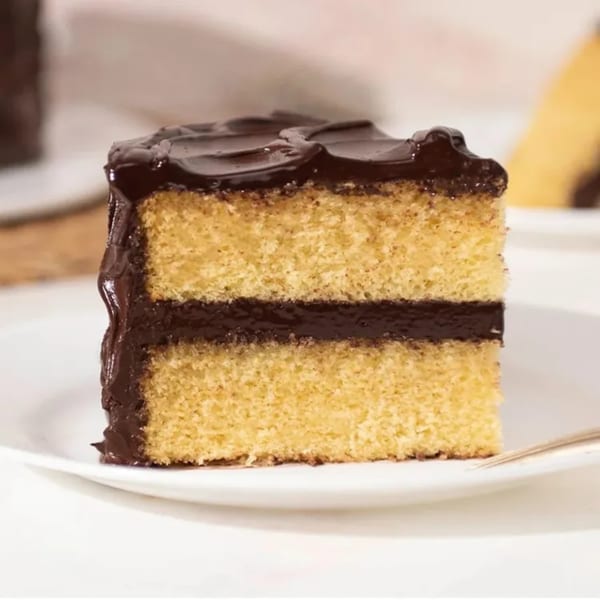 A slice of yellow cake with chocolate frosting between layers and on top, on a white plate.
