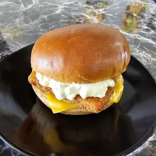 Ray's Chicken & Fish's fried fish sandwich with tartar sauce and cheese on a black plate.