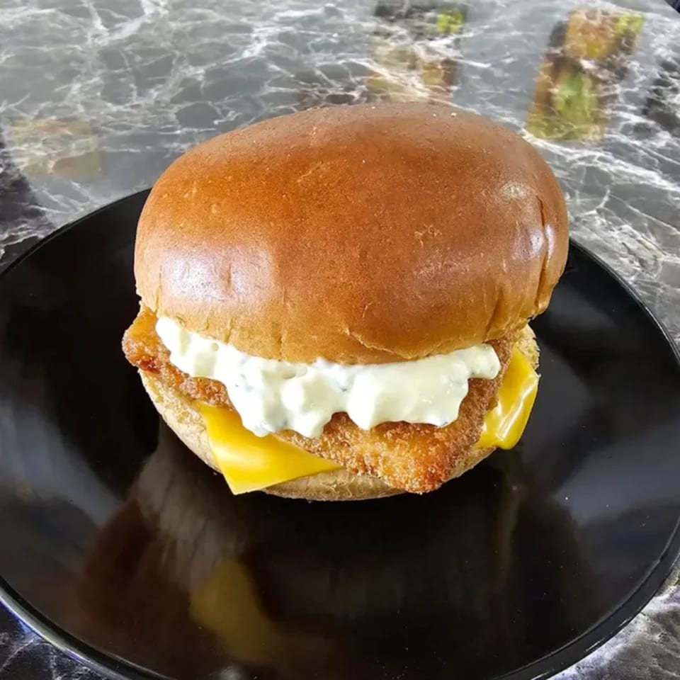 Ray's Chicken & Fish's fried fish sandwich with tartar sauce and cheese on a black plate.